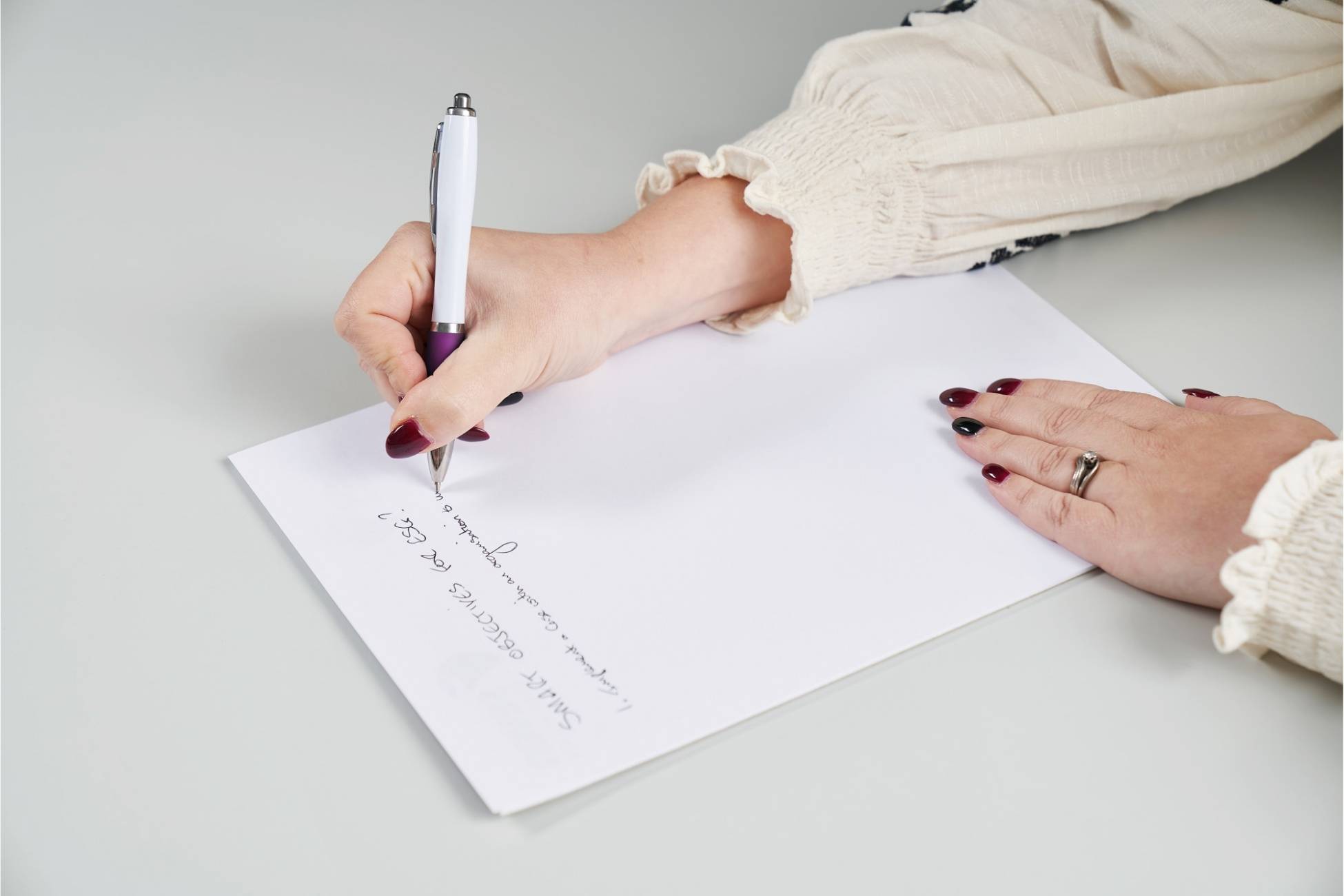 A female hand writing with a pen on a sheet of white paper.